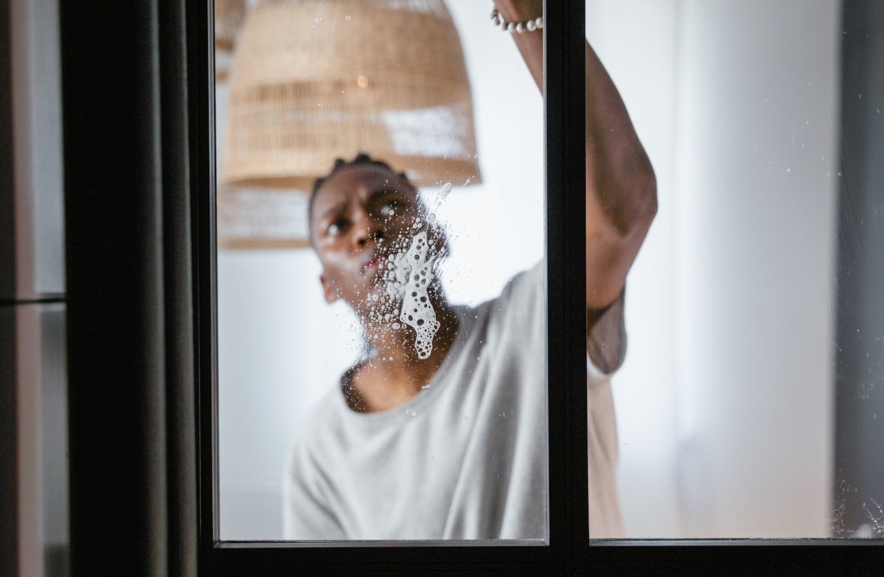 about-02 An adult male cleaning a glass window indoors, focusing on household chores and cleanliness.
