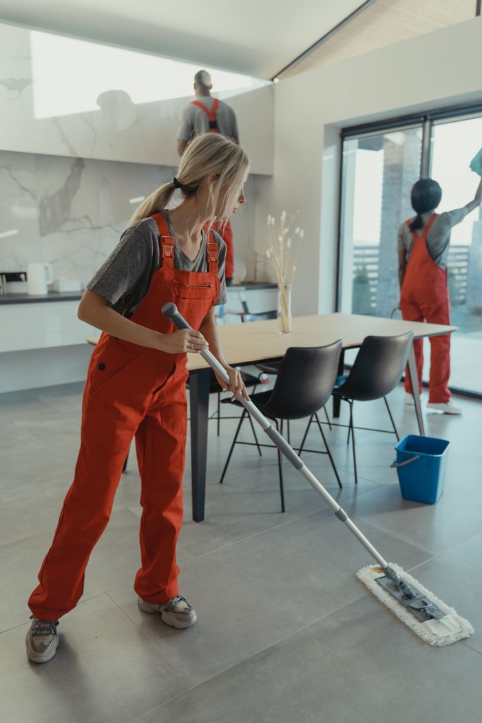hero-img-01 Cleaning team in red overalls mopping and sanitizing a modern home interior.