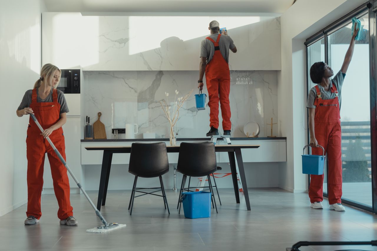 hero-img-02 Group of cleaners in red uniforms mopping and wiping glass in a modern dining room.